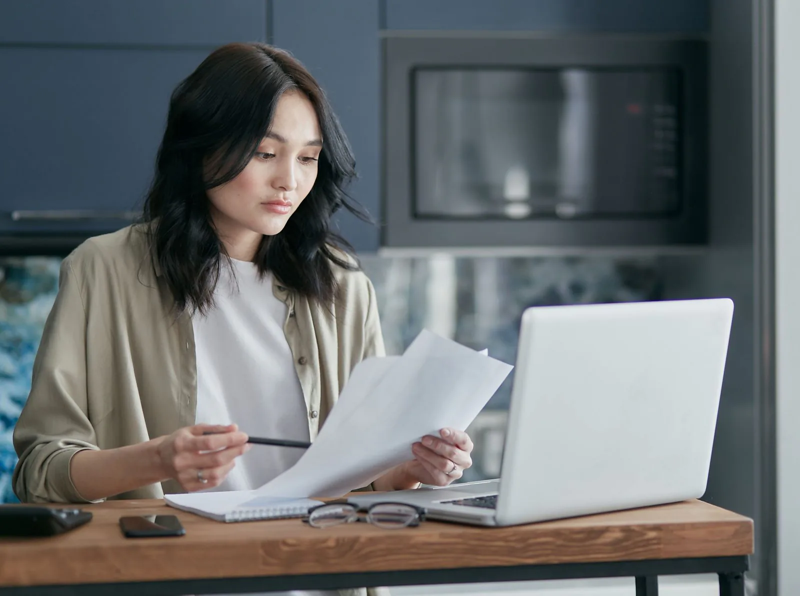 Dona de restaurante revisa documentos fiscais junto ao notebook na cozinha